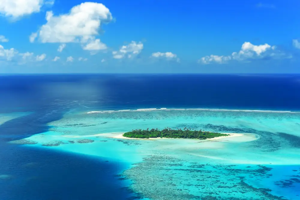 A reef drop-off a few metres from a white Maldivian beach with overwater villas beyond